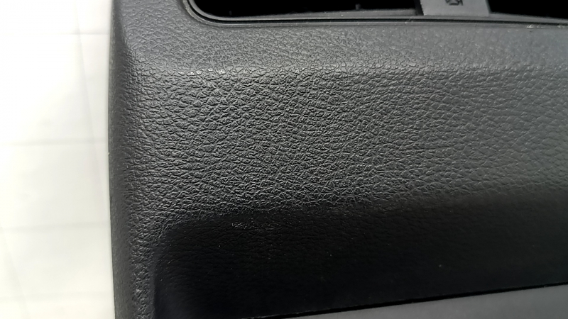 Ближний план черной накладки центральной консоли Nissan, заметные царапины на поверхности.