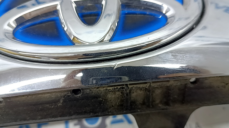 Детальный крупный план области логотипа Toyota, видны потертости и небольшая царапина.