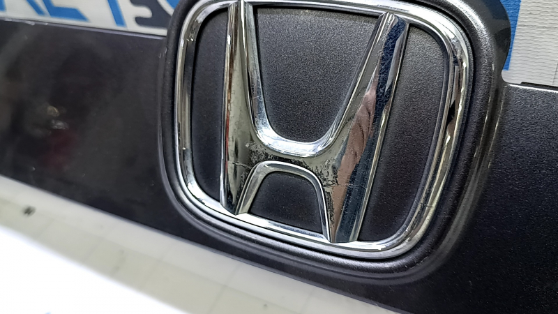 Крупный план эмблемы Honda на молдинге, видимые повреждения