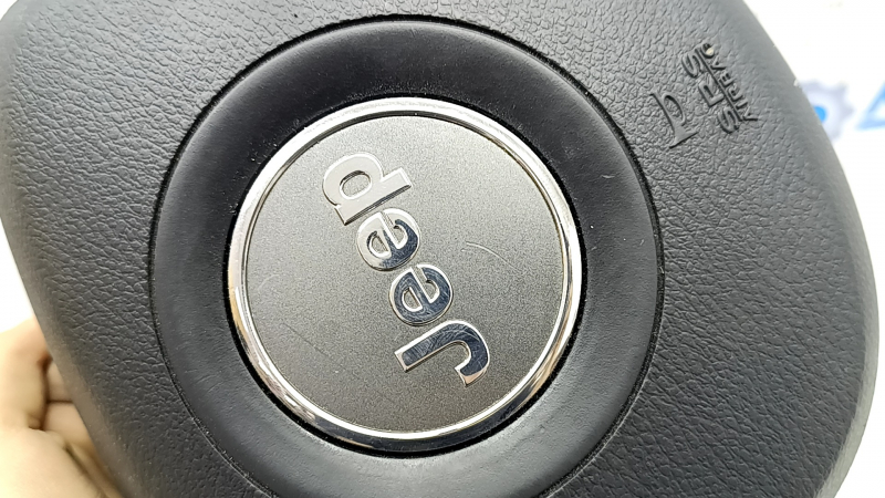 Крупный план логотипа Jeep на подушке безопасности, заметны следы использования.