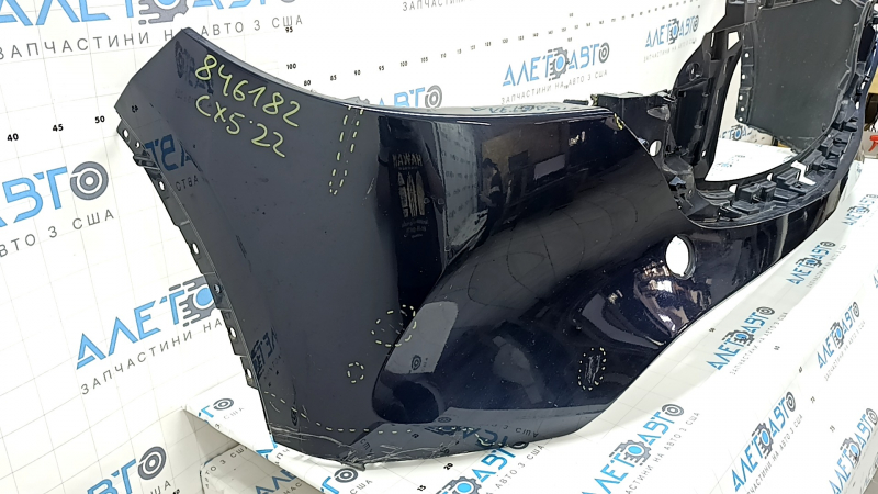 Крупный план боковой части переднего бампера Mazda CX-5 с заметными дефектами, видна надорванная область.