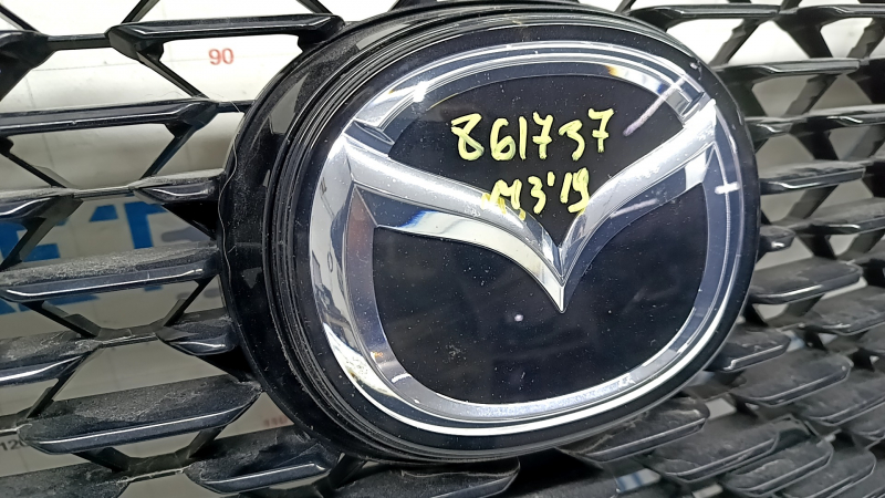 Эмблема на решетке радиатора Mazda 3 2019; оригинал с номером 861737; вид спереди.