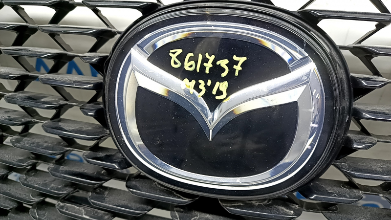 Детали эмблемы на решетке радиатора Mazda 3 2019; вид сбоку, низкие потертости.