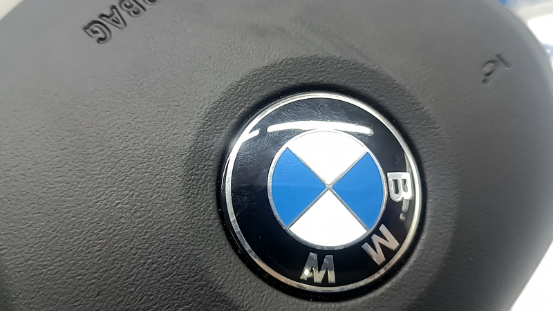 Крупный план логотипа BMW на подушке безопасности рулевого колеса.