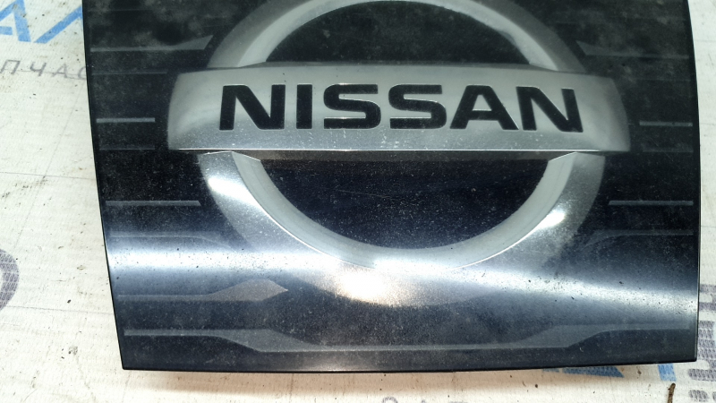 Ближайший ракурс эмблемы радиатора Nissan с видимыми потертостями.
