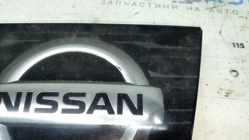 Детальный снимок эмблемы Nissan, показывающий повреждения и следы эксплуатации.
