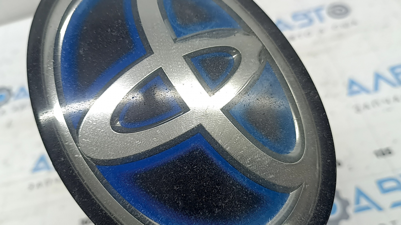 Крупный план эмблемы решетки радиатора Toyota, видны трещины на покрытии.